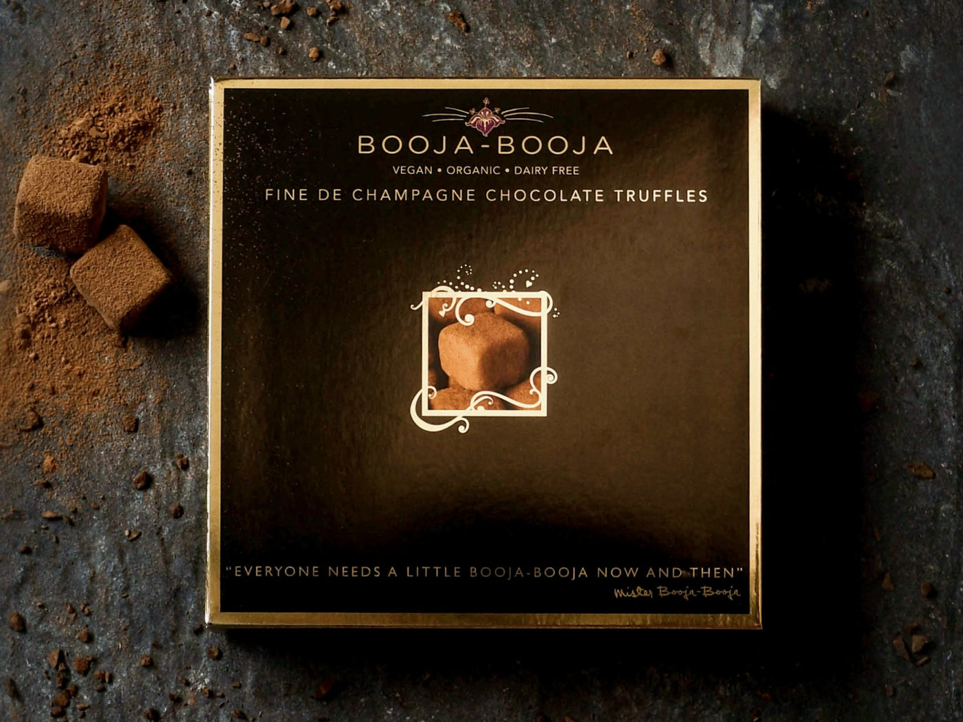 The Booja-Booja Fine De Champagne 138g gift box, photographed on a slate background with loose truffles around